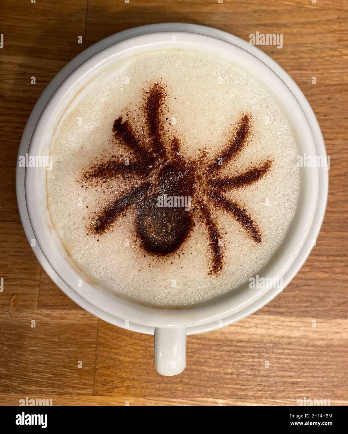 A mug of frothy cappuccino coffee has a spider image in the froth made of chocolate sprinkles.Viewed from above.Halloween symbol of All Hallows Eve Stock Photo