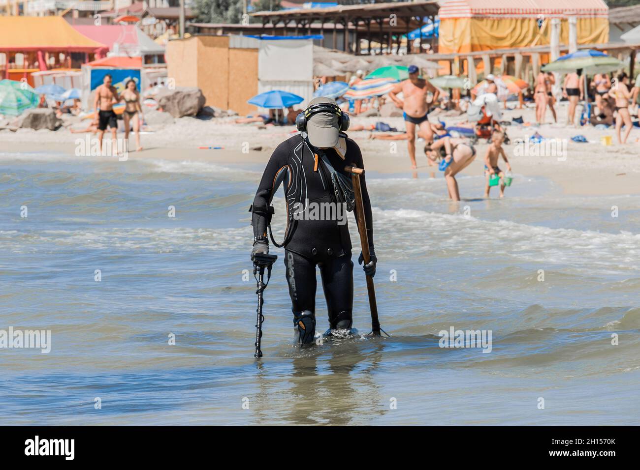 A man with a special device and equipment metal detector looking for lost jewelry and gold in sea water near the beach. Stock Photo
