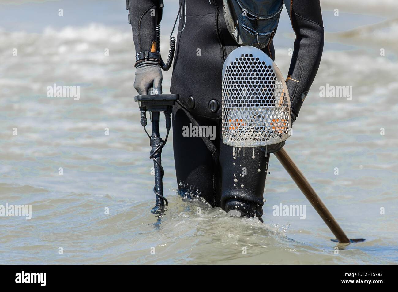 A man with a special device and equipment metal detector looking for lost jewelry and gold in sea water near the beach. Stock Photo