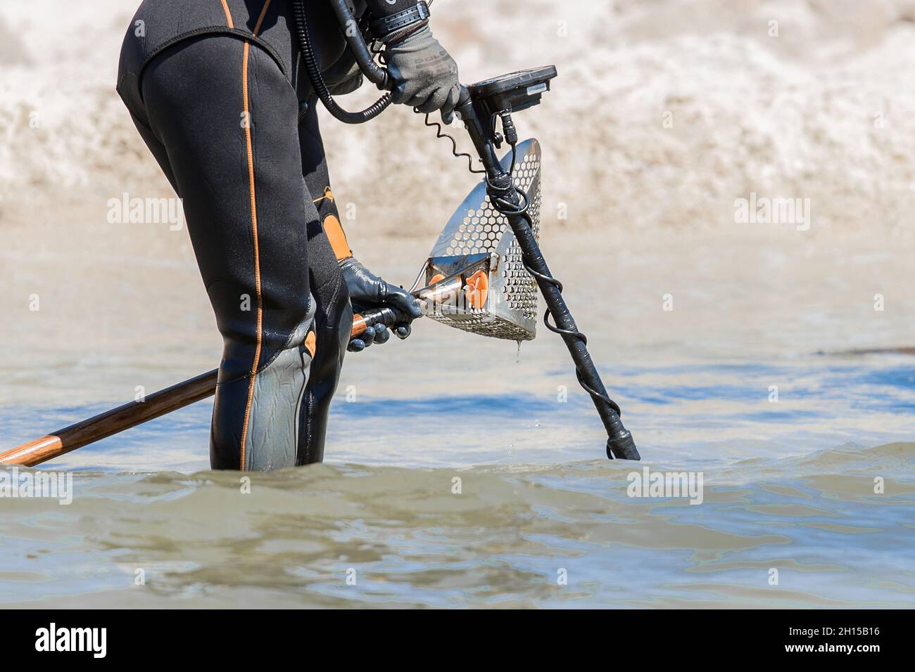 A man with a special device and equipment metal detector looking for lost jewelry and gold in sea water near the beach. Stock Photo