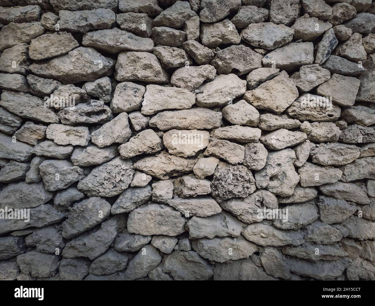 Irregular stone masonry wall background. Old limestone rocks of different size and shapes stacked carefully. Detailed texture of construction element. Stock Photo
