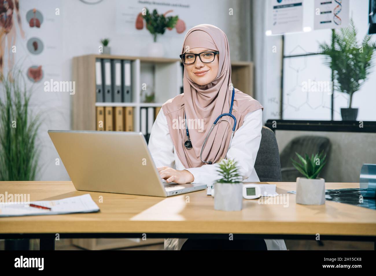 Pretty woman in hijab and eyeglasses sitting at desk and typing in ...