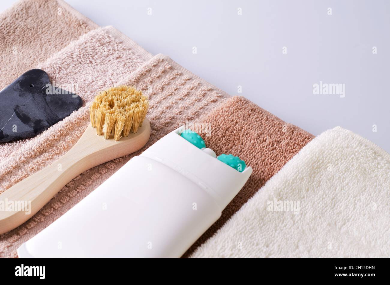 Lifting cream in tube with massage roller nozzle close-up, brush made of natural bristles and gouache made of natural stone for a stack of towels Stock Photo