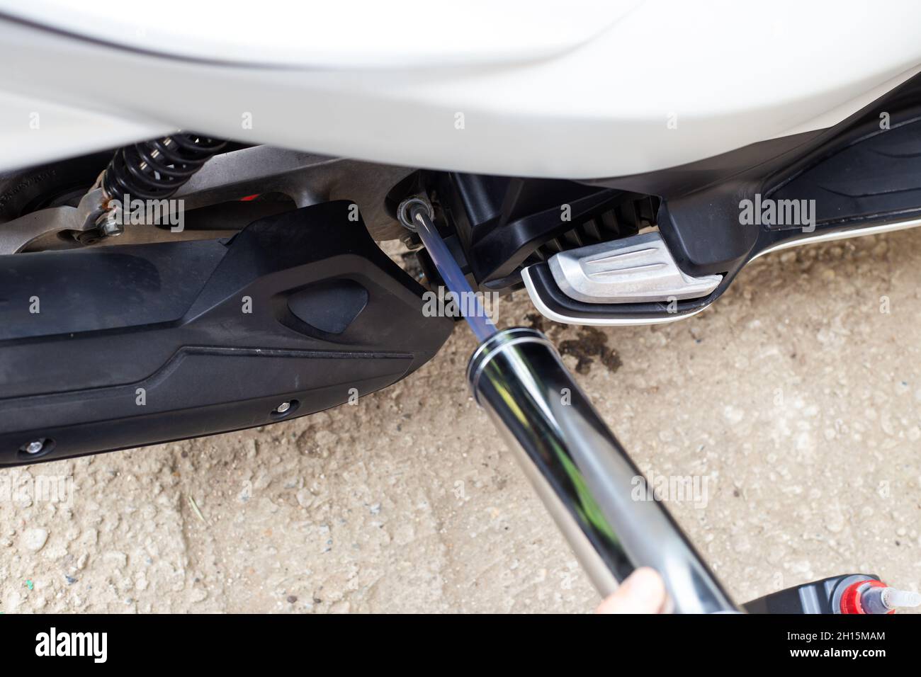 Pouring engine oil into a motorbike engine using a metal syringe. Oil
