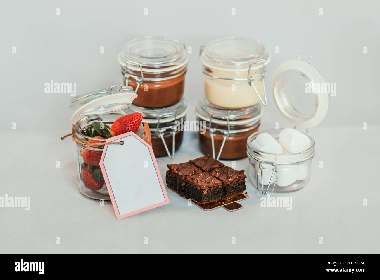 Opened transparent isolated jars with price tag and strawberry on table with sweet delicious dessert inside on white background Stock Photo