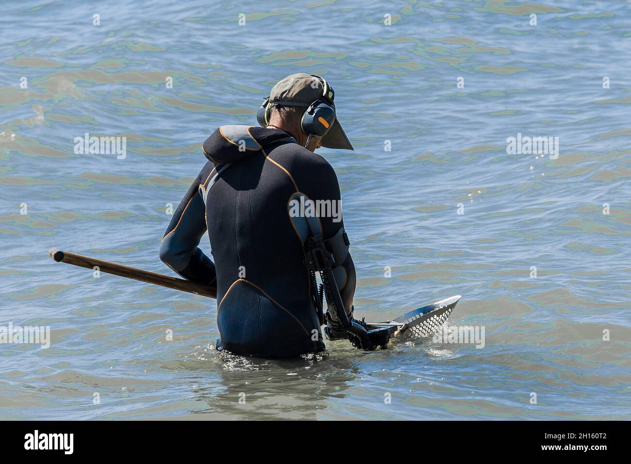 A man with a special device and equipment metal detector looking for lost jewelry and gold in sea water near the beach. Stock Photo
