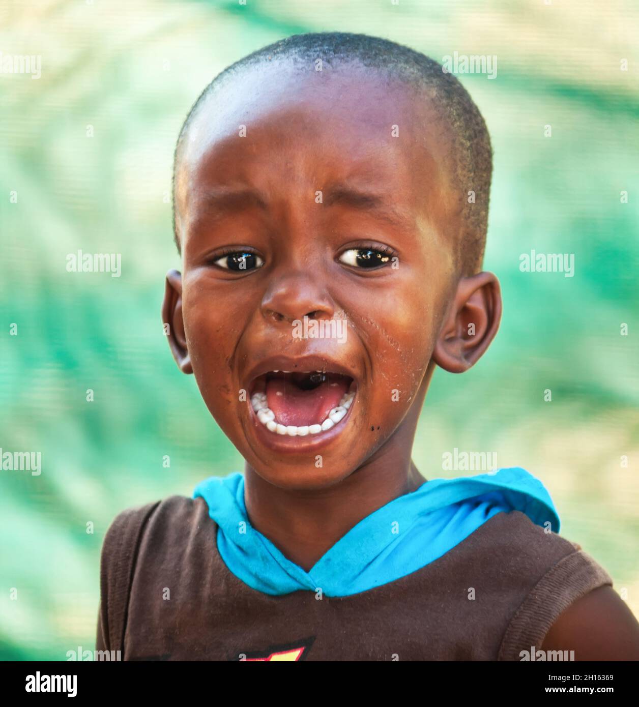 African child portrait in a village in Botswana standing in front of the green fence in the yard, crying Stock Photo