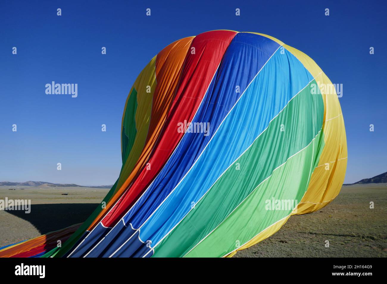 Deflating rainbow colored hot air balloon falling away Stock Photo