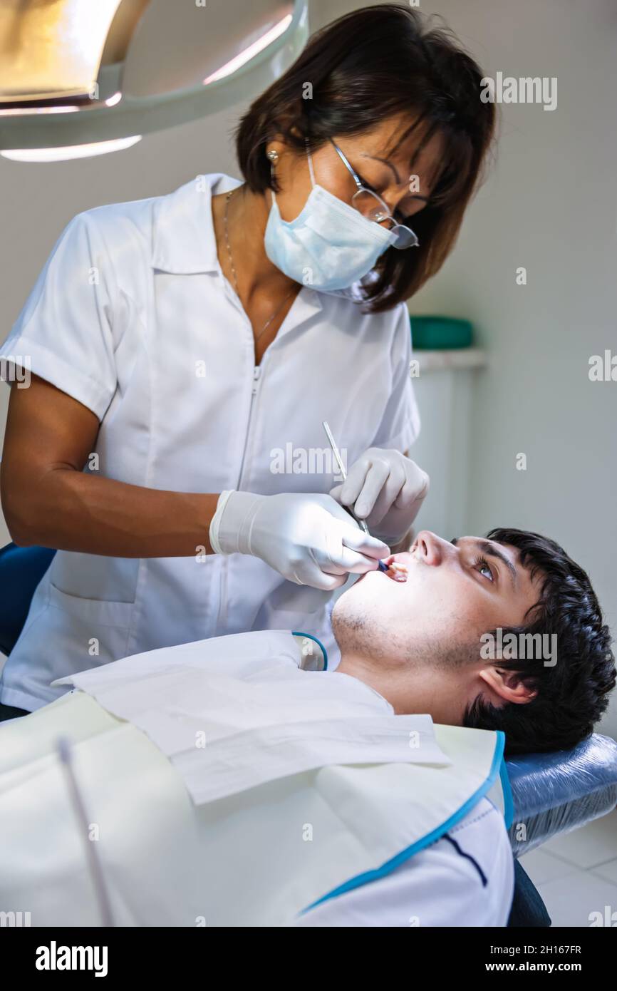 South American dentist checking up the teeth of a young Caucasian man Stock Photo