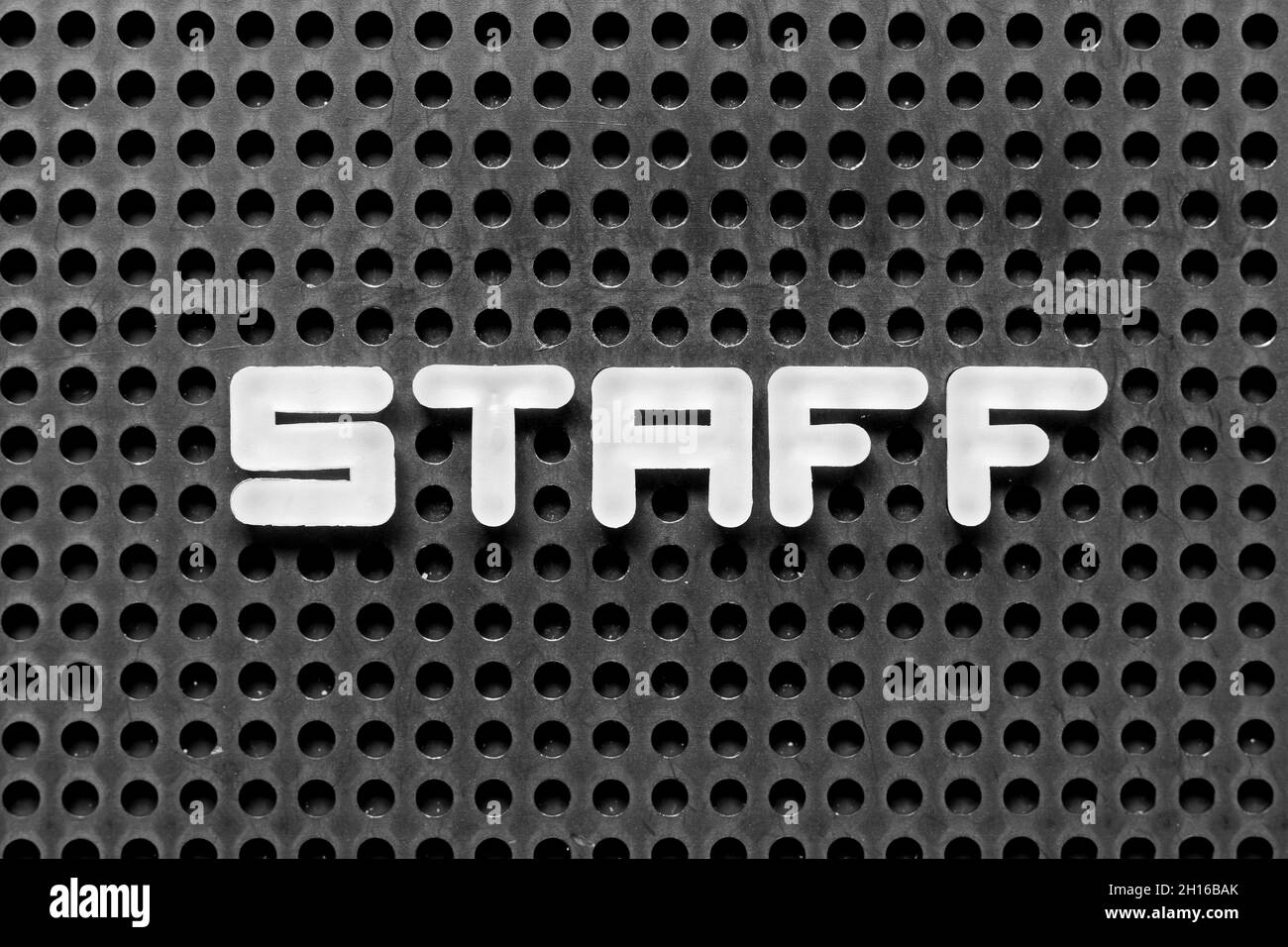 White alphabet letter in word staff on black pegboard background Stock