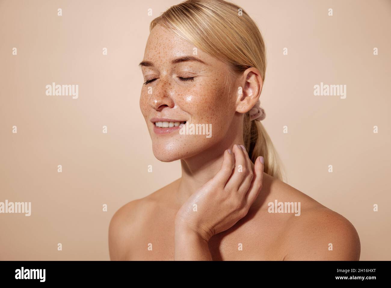 Smiling woman with freckles and perfect skin massaging her neck against pastel background Stock Photo