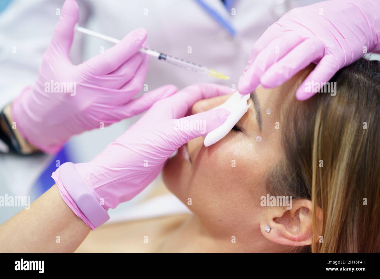 Aesthetic doctor injecting botulinum toxin into the forehead of her middle-aged patient. Stock Photo