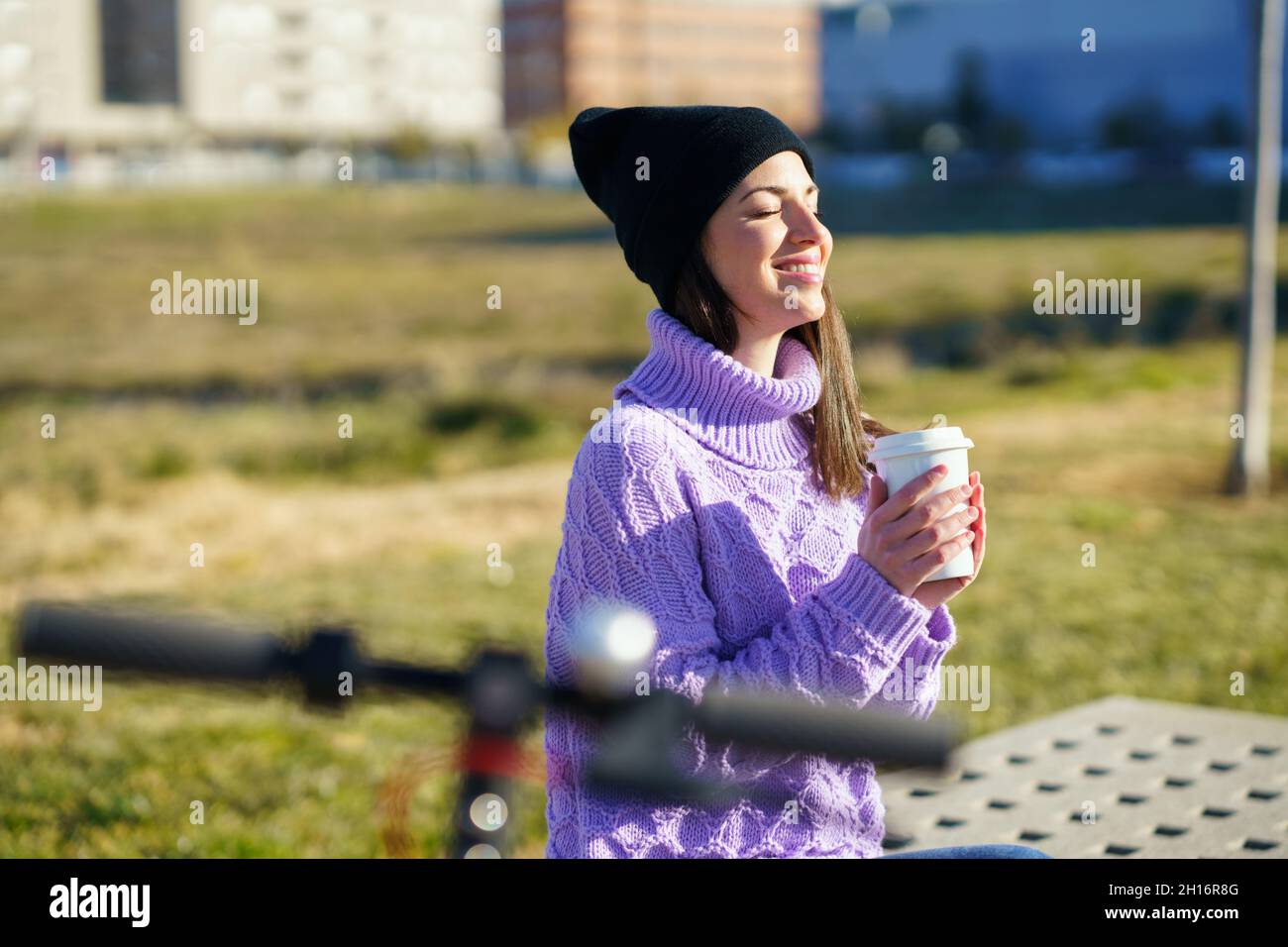 Female student with electric scooter enjoying the winter sunlight with her eyes closed. Stock Photo