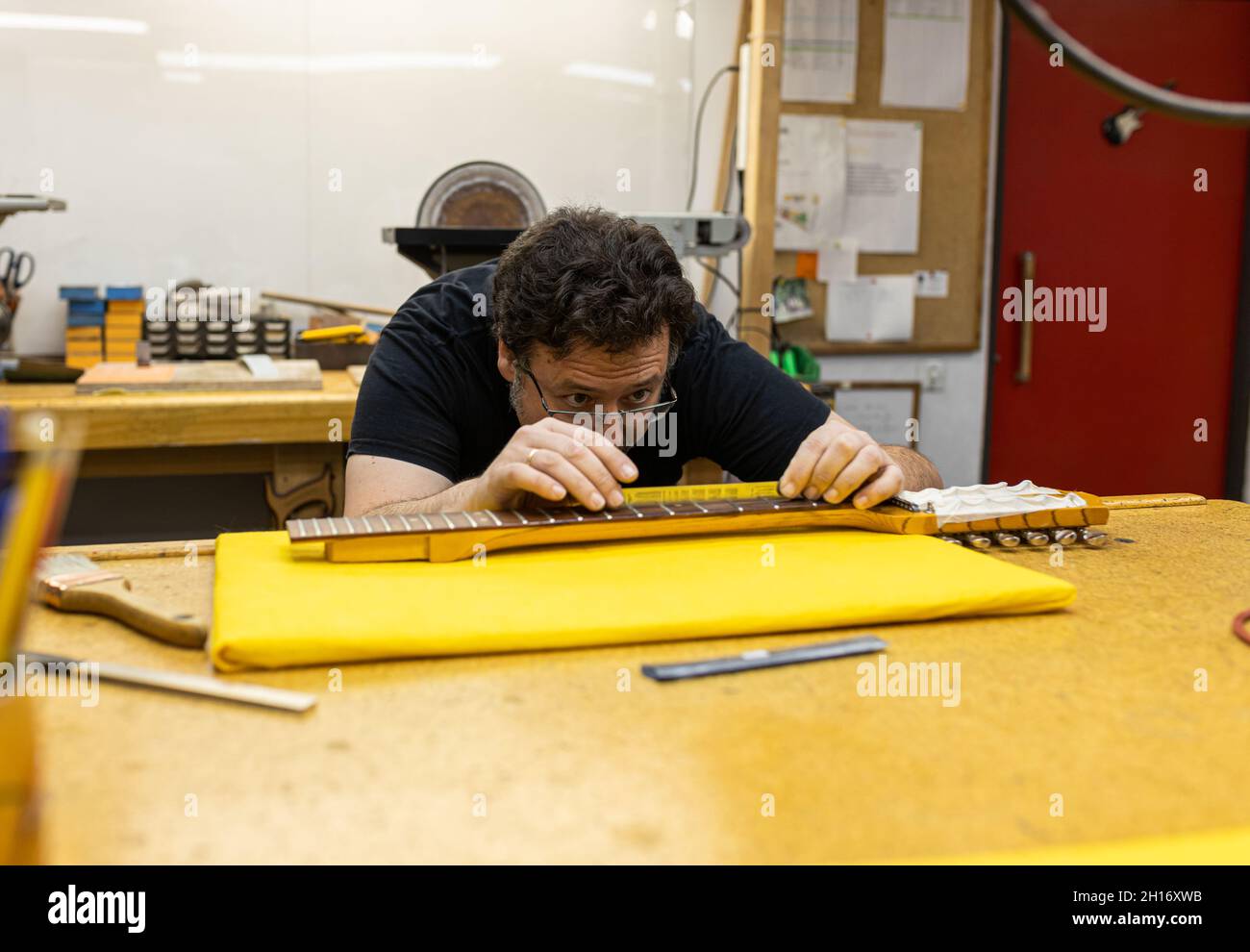 Concentrated craftsman in eyeglasses measuring distance between frets