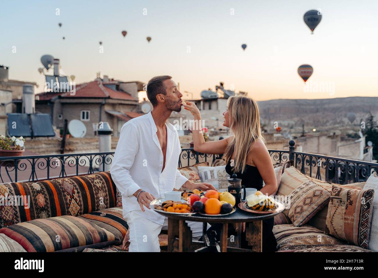 Er is behoefte aan Bijwerken team Couple holding hands and looking at each other while enjoying romantic  dinner and feeding each other with fruits on terrace with hot air balloons  on b Stock Photo - Alamy