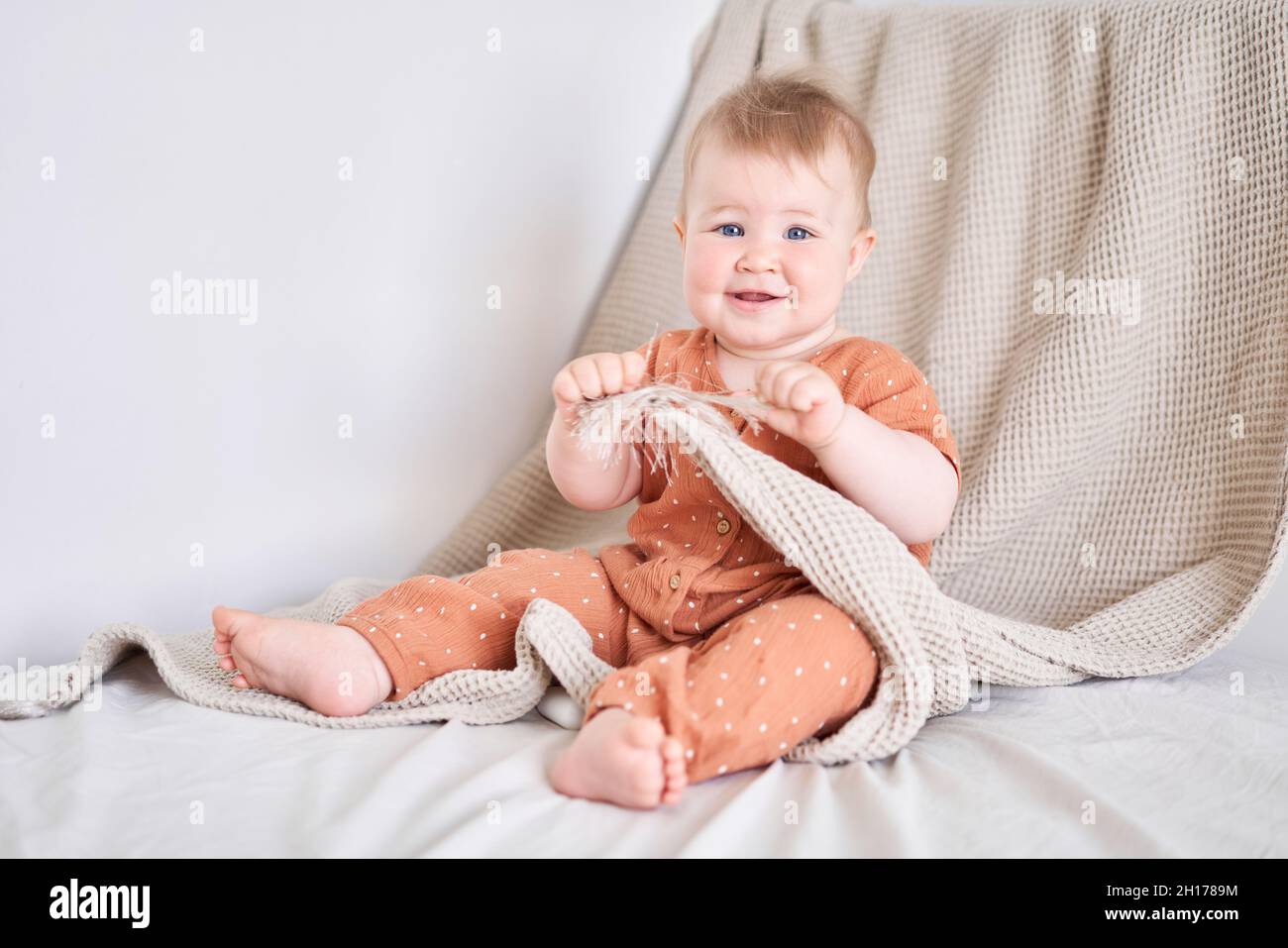 Portrait of a cute 9 months old baby girl seating on a bed. Stock Photo
