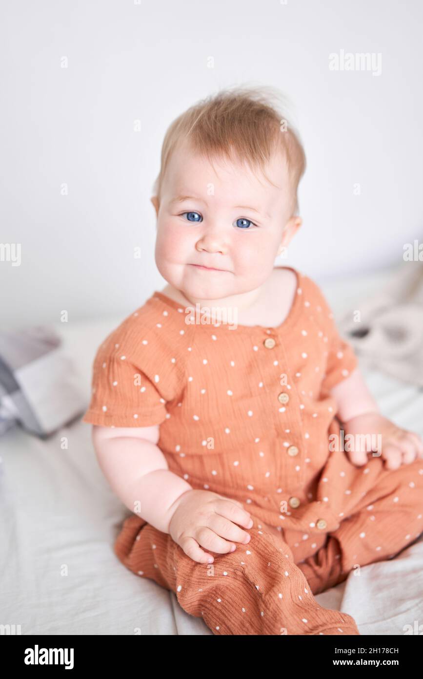 Portrait of a cute 9 months old baby girl seating on a bed Stock Photo