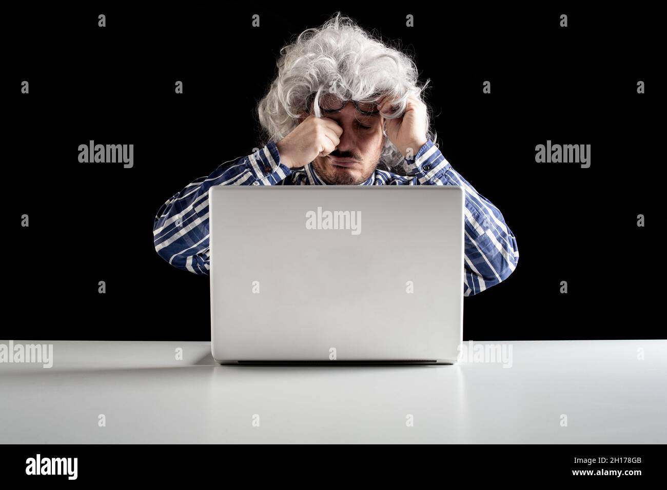 Portrait of a senior man rubbing his tired eyes sitting in front of the ...