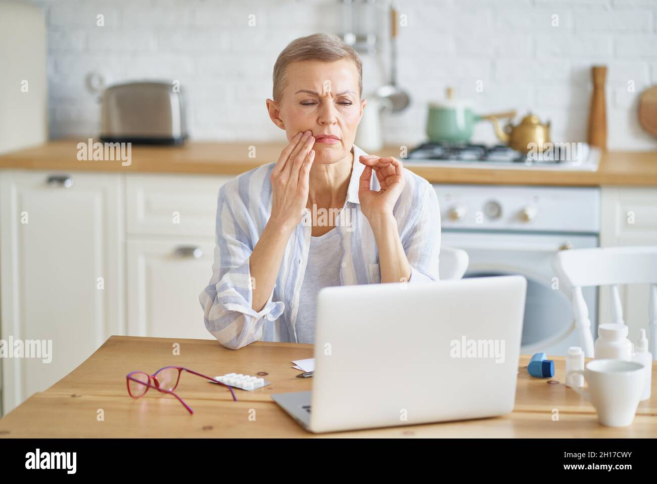 Frustrated mature woman suffering from toothache while working online from home Stock Photo