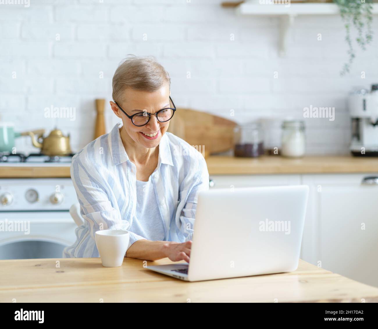 Happy middle aged woman typing something on keyboard while working or studying on laptop at home Stock Photo