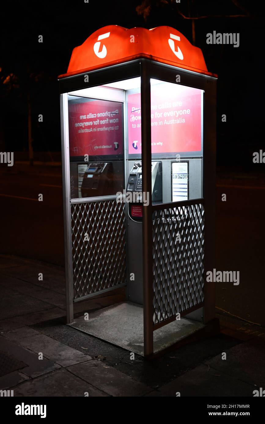 A Telstra payphone at night, with signature orange illumination on the top of the booth Stock Photo