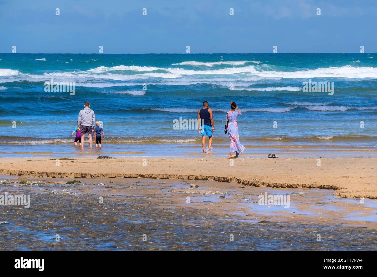 Mawgan Porth beach in Cornwall, holidaymakers standing on the shoreline enjoying the view on their staycation Cornish holiday. Stock Photo