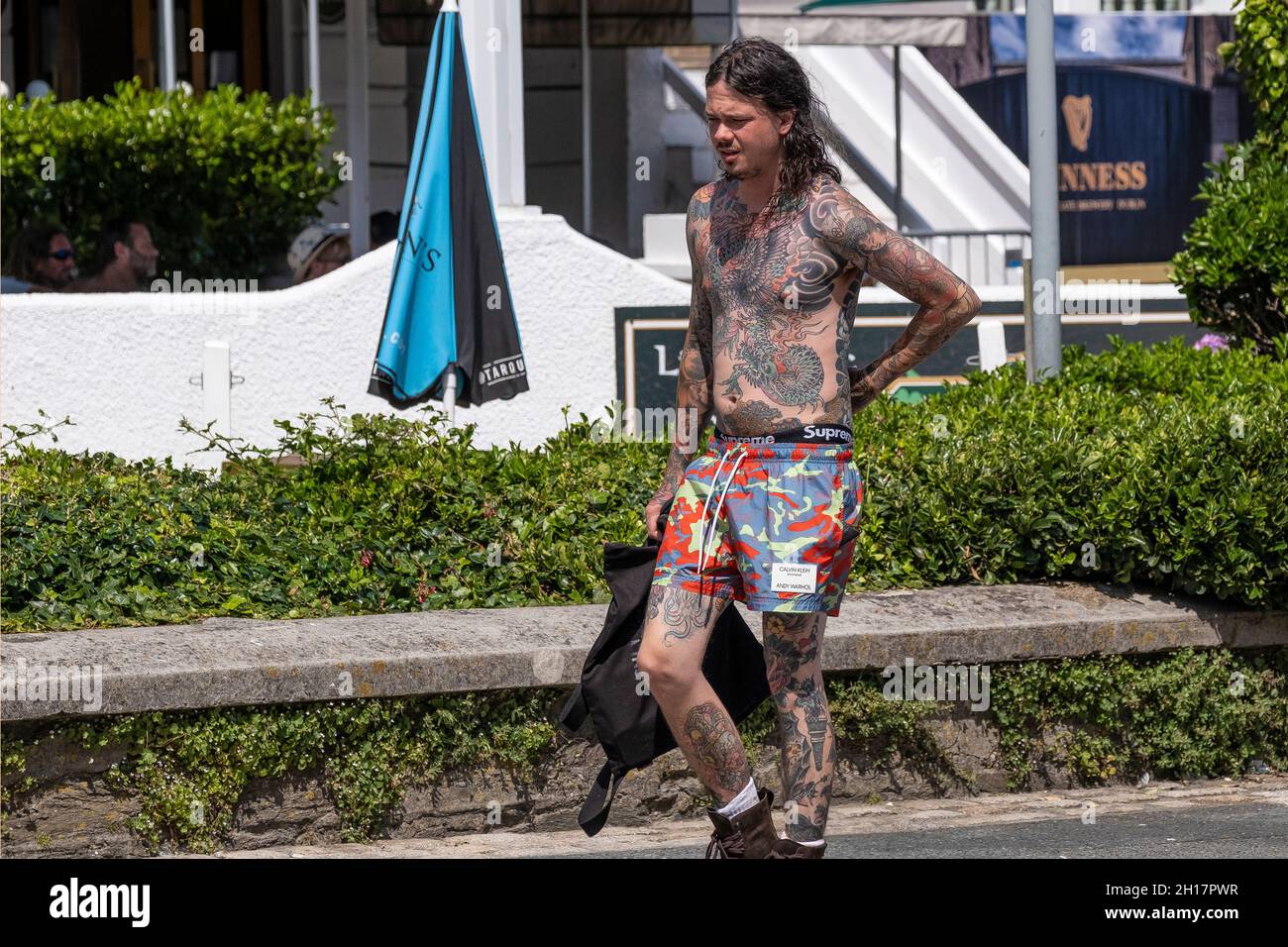 A young man heavily tattooed with Japanese style tattoos Irezumi walking in a sunny Newquay Town centre in Cornwall. Stock Photo