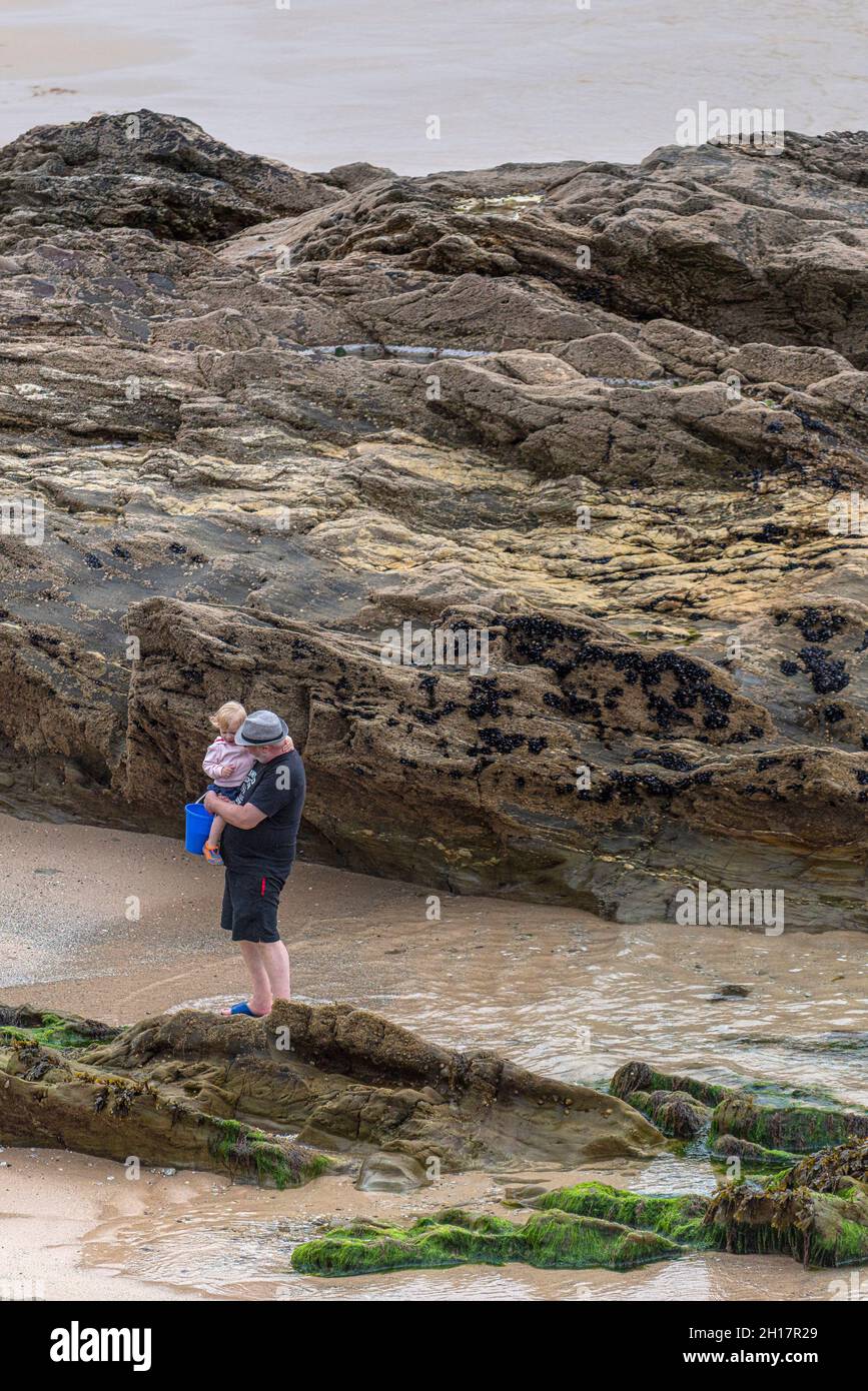A grandfather carrying his granddaughter exploring the inter tidal zone at low tide on Fistral Beach in Newquay in Cornwall. Stock Photo