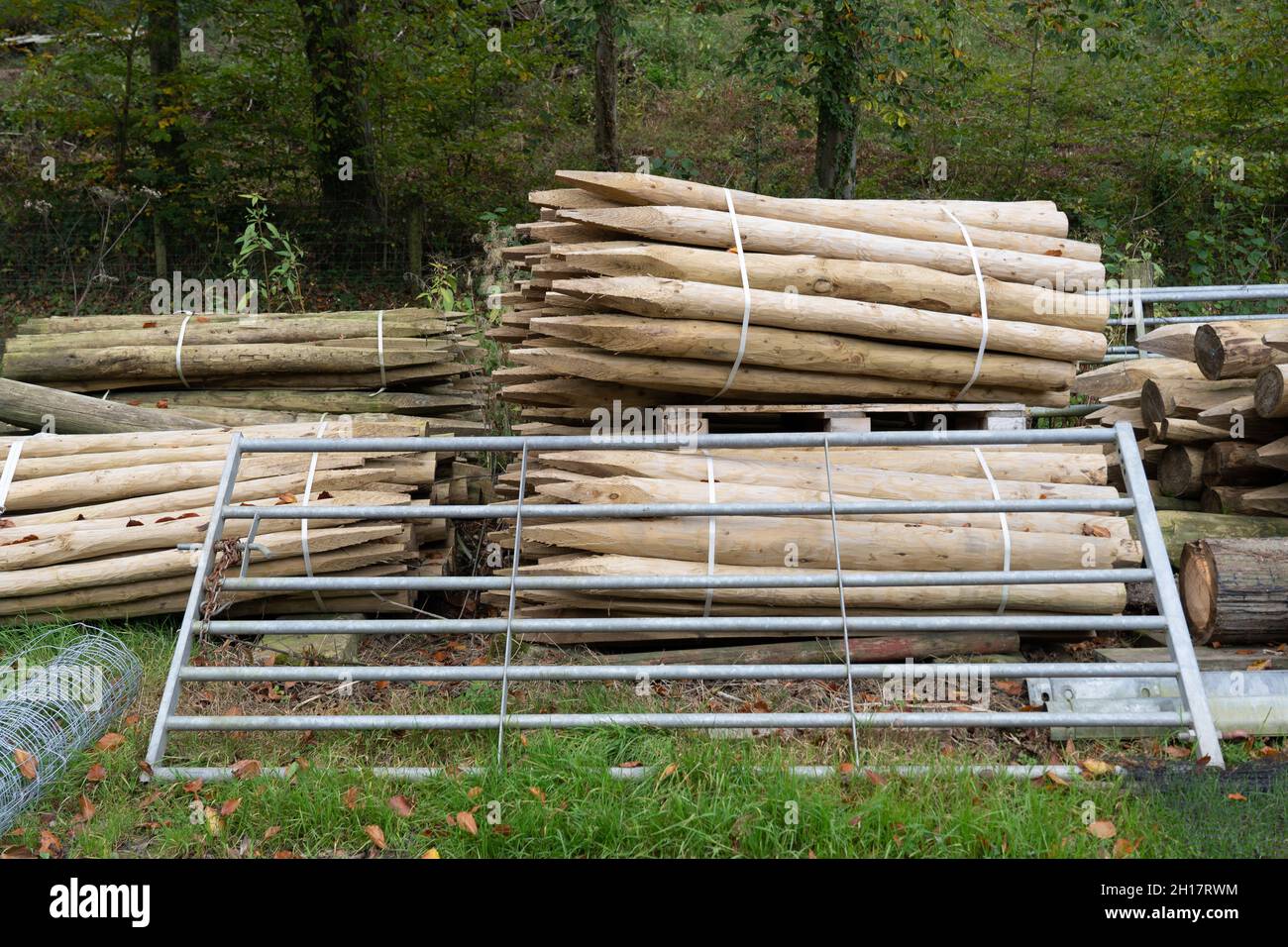 bundles of Wooden fence posts, round wood piles and galvanised metal