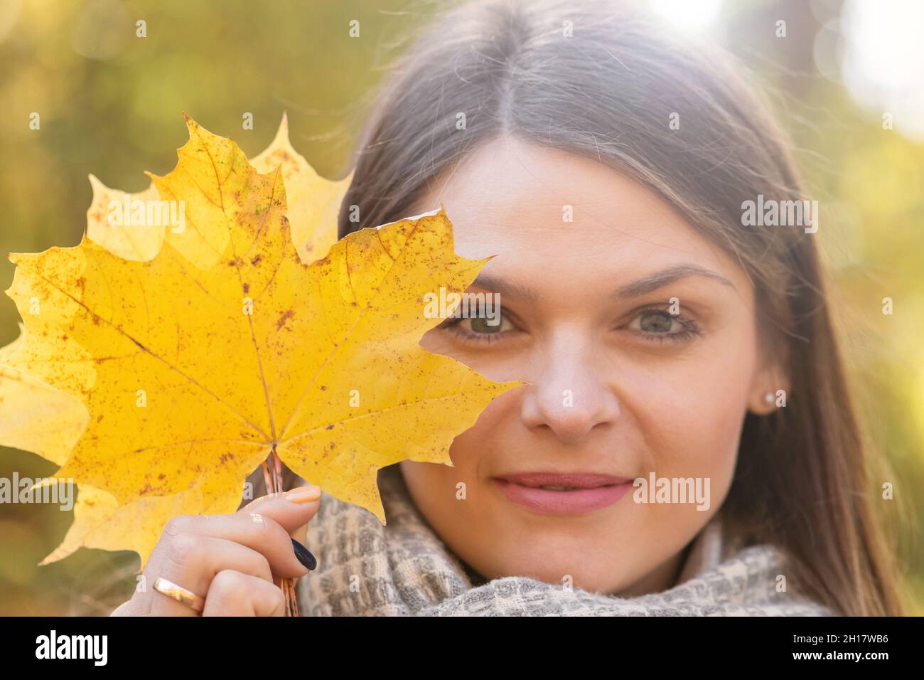 Portrait of brunette woman with yellow maple tree leaf cover her face ...