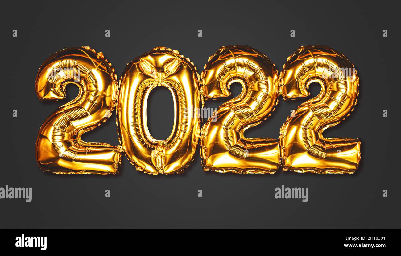 Happy New year 2022 celebration. Bright gold balloons figures New Year Balloons with glitter stars on dark background. Christmas and new year Stock Photo