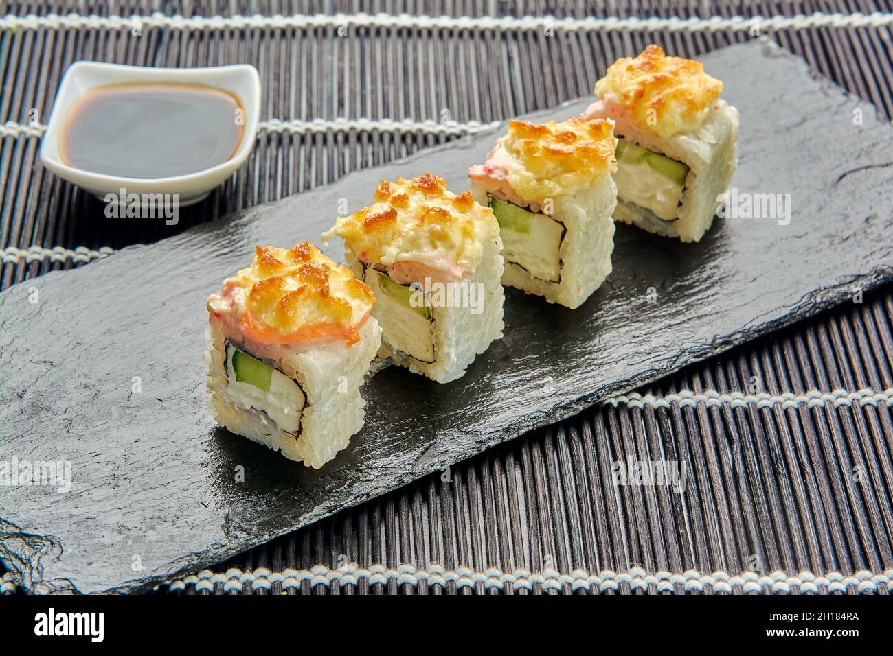Baked cucumber rolls on a dark stone. Japanese sushi. Stock Photo