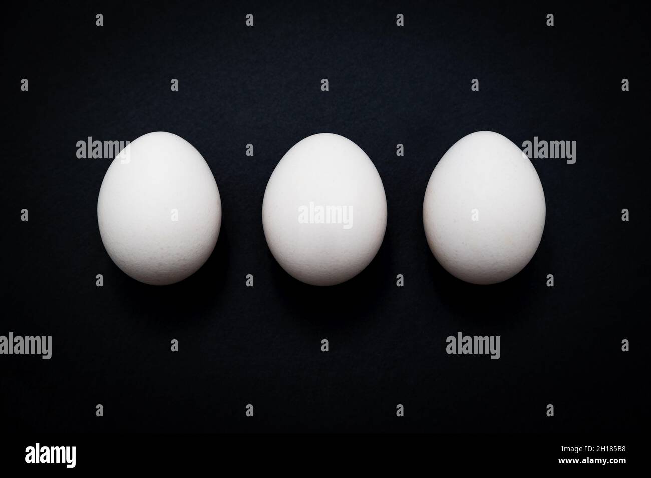 Horizontal breakfast triple: three white chicken eggs against a dark slate background. Stock Photo