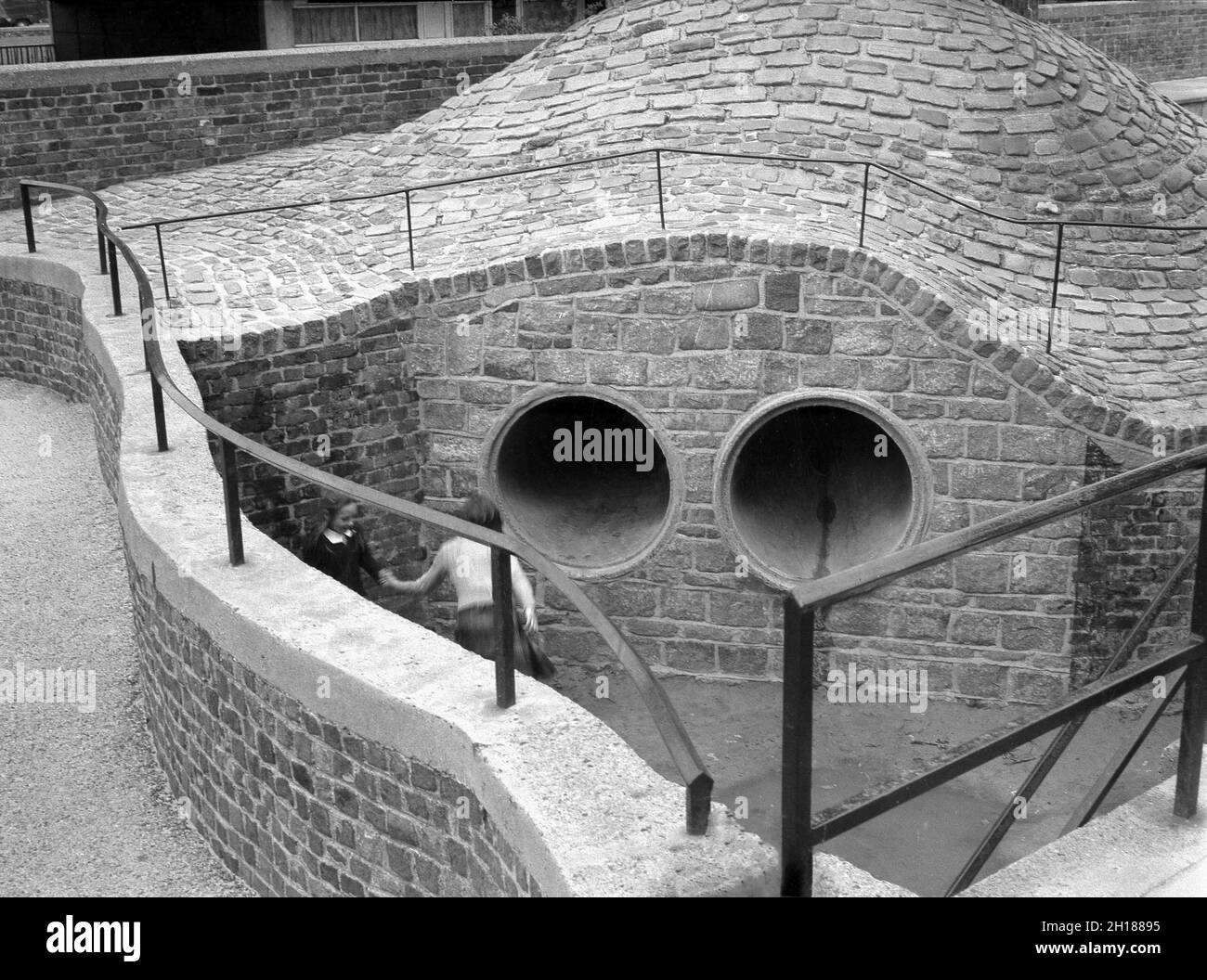 1960s, historical, two young children playing at a curved concrete and ...