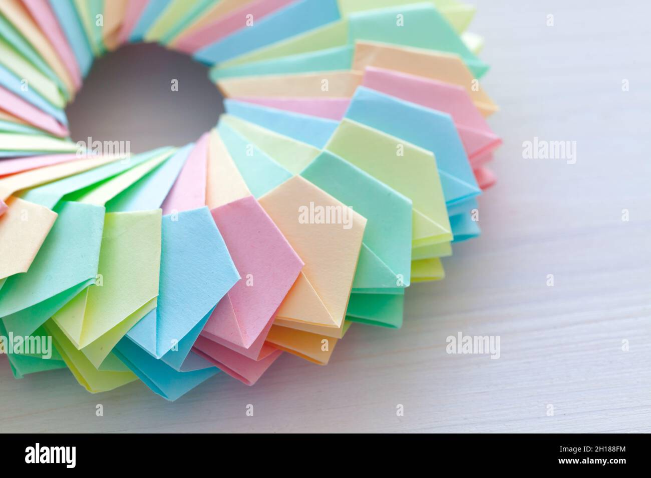 Origami, fragment of an abstract parametric ring made of colorful paper sheets lay on a white desk, top view Stock Photo