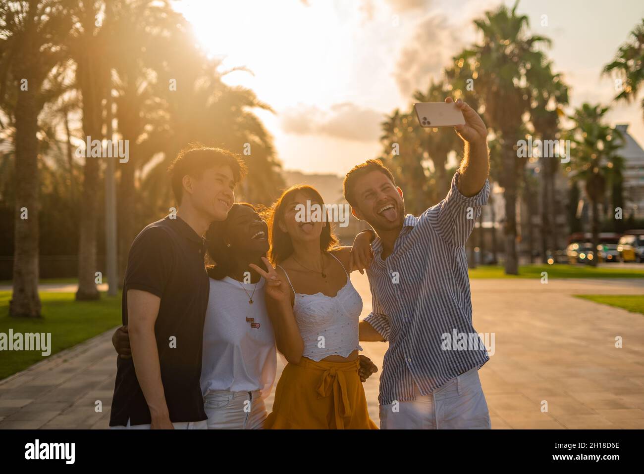 Group of delighted young multiracial people making funny faces while taking selfie on smartphone during meeting in tropical city in sunny summer evening Stock Photo