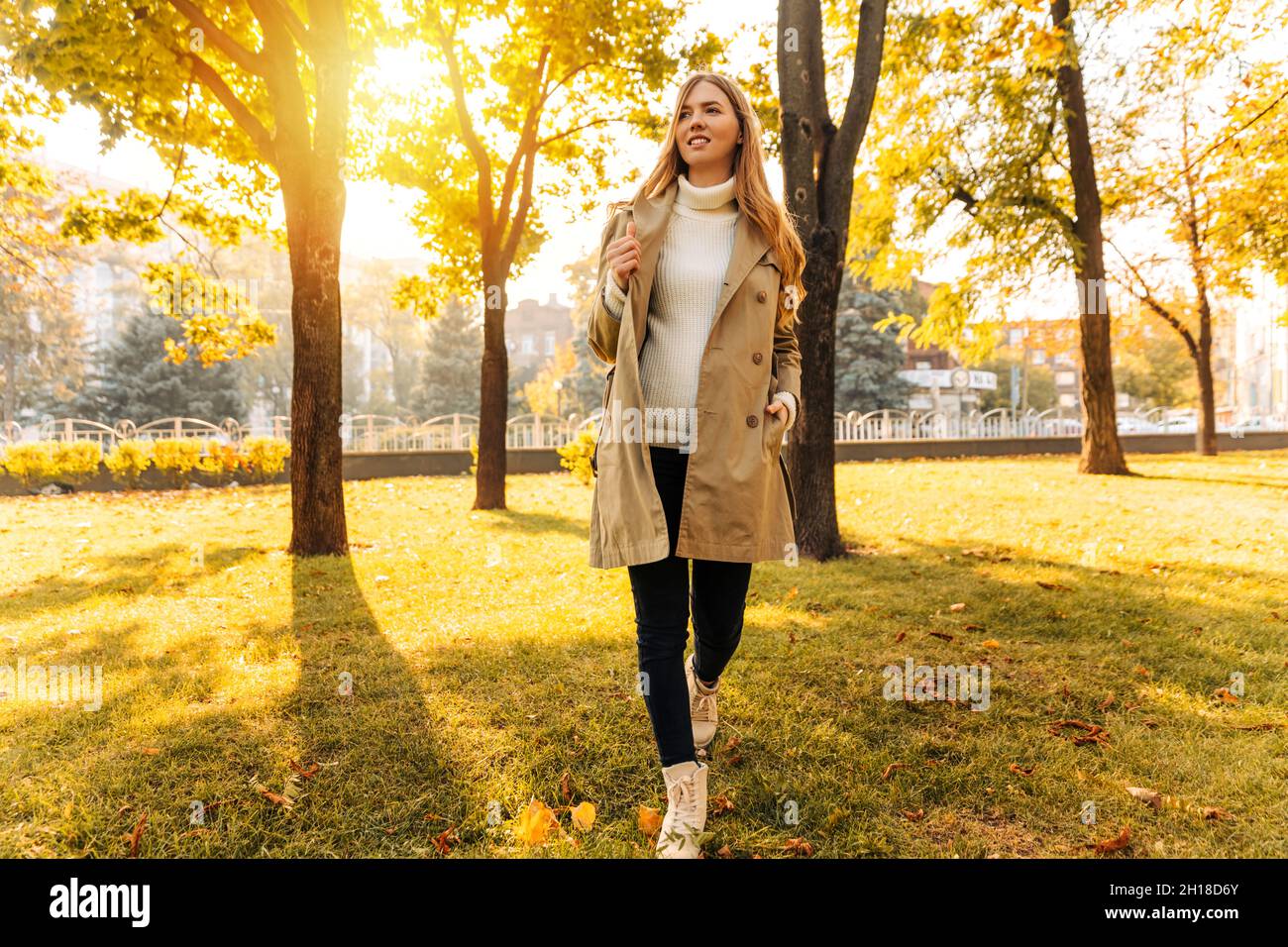beautiful woman in a beige raincoat sits on the grass in the park ...