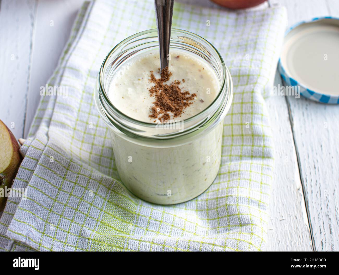 Homemade yogurt with pureed red apple and cinnamon topping served on white background with spoon. Stock Photo