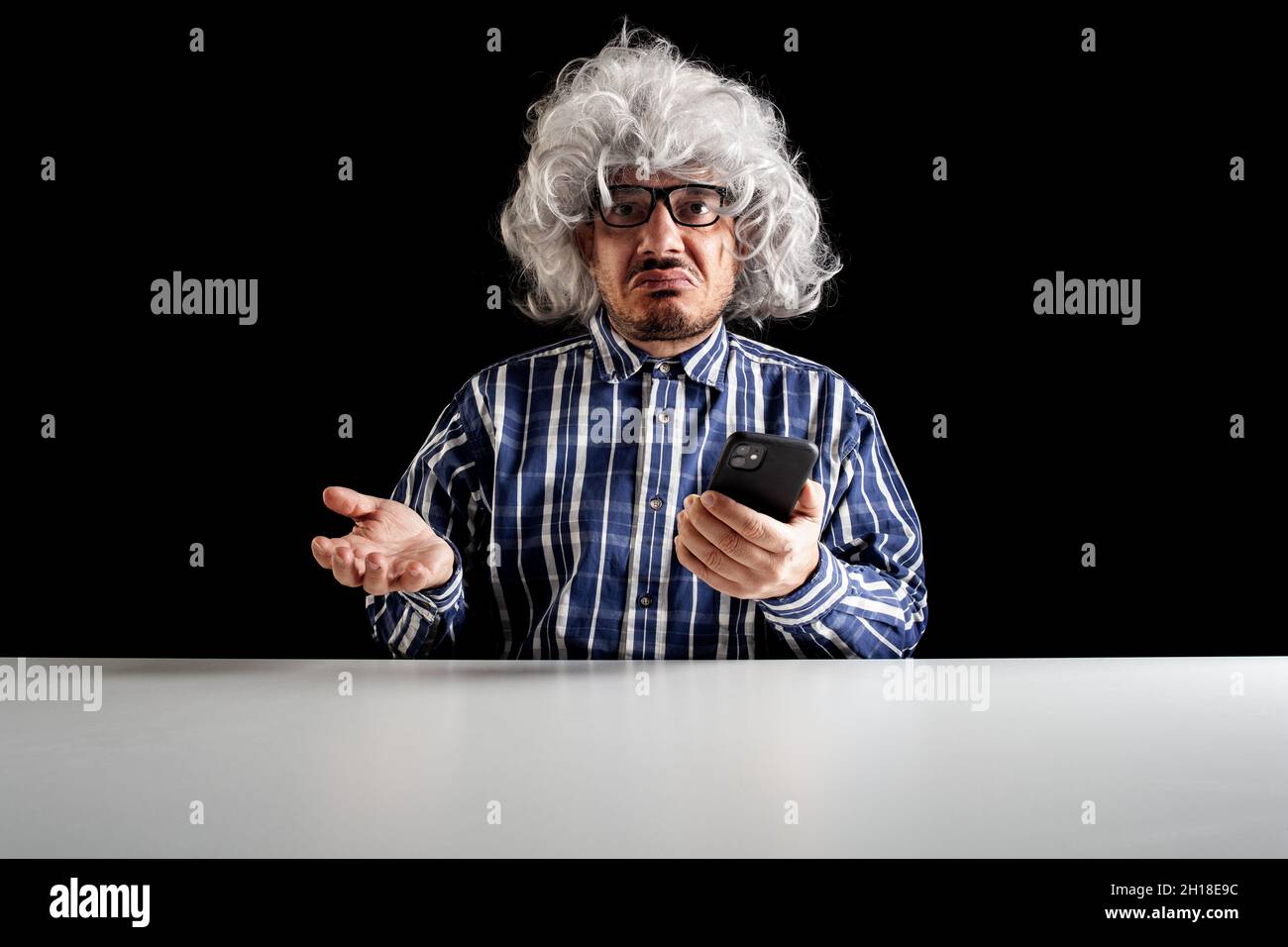 A bewildered senior, typical boomer,  does not understand how to use the smartphone on black background Stock Photo