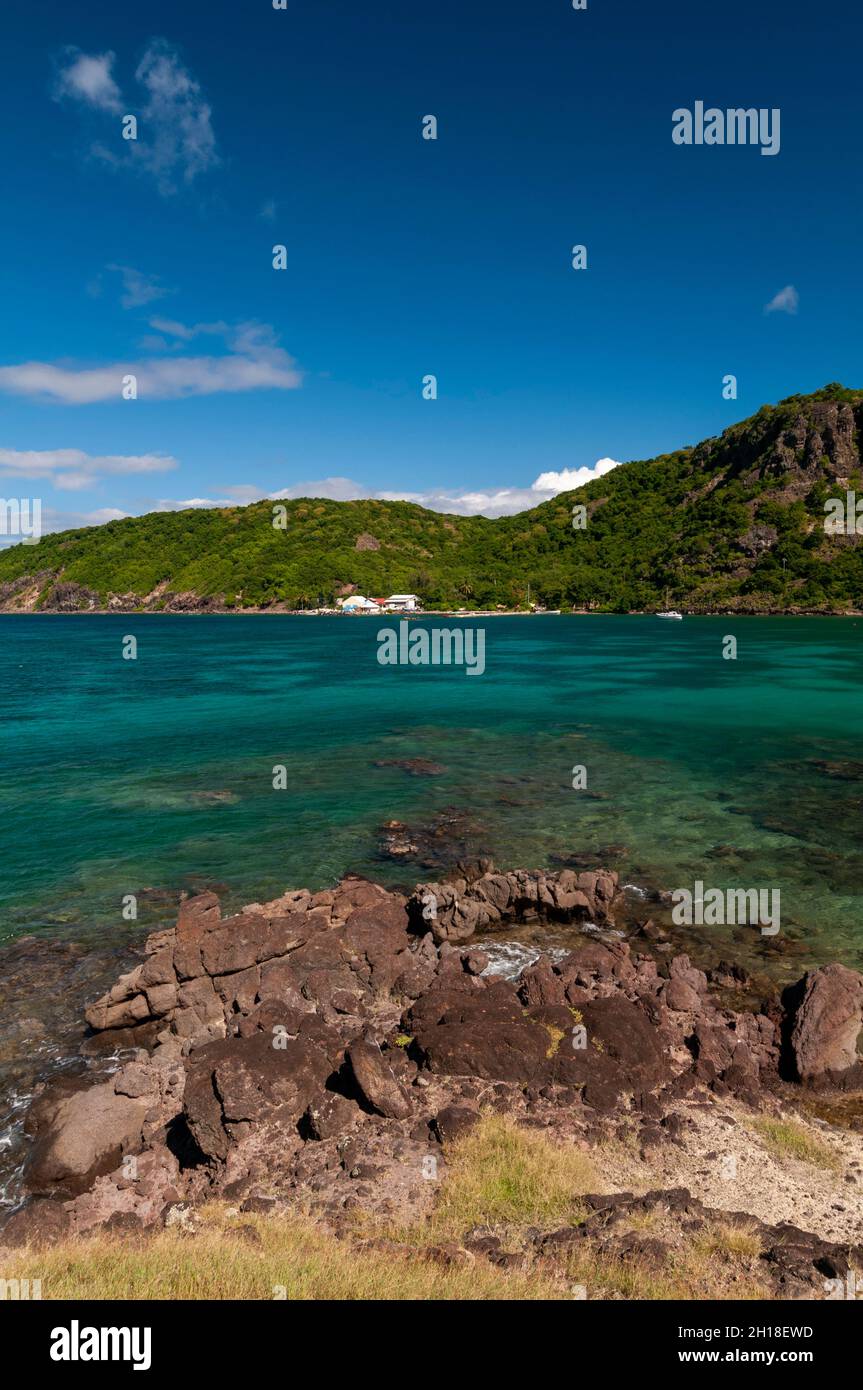 A rock shoreline borders the clear tranquil waters of Marigor Bay. Terre de Haut, Iles des Saintes, Guadeloupe, West Indies. Stock Photo