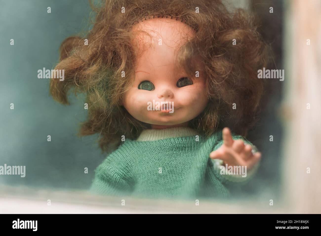 Close-up of an old doll peeking through the window. Halloween concept Stock Photo