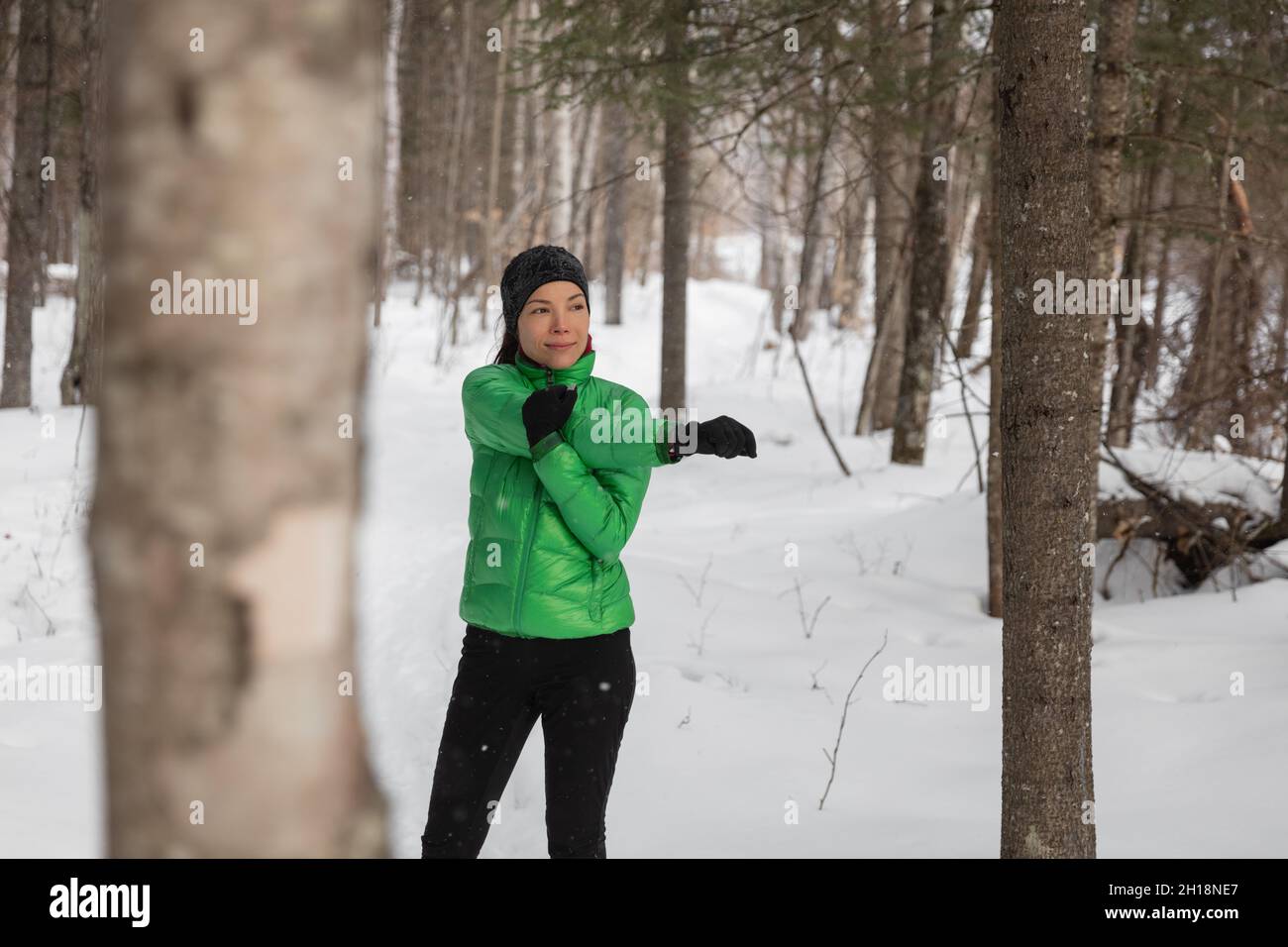 Winter fitness athlete woman warming up stretching arms before her outdoor run running on snow trail. Asian runner wearing cold weather gloves Stock Photo
