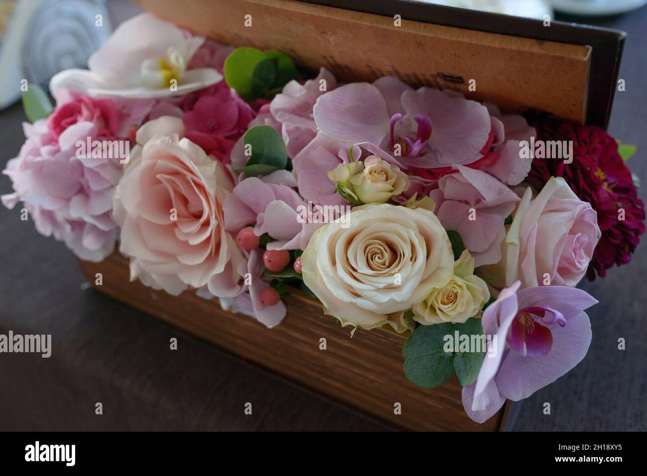 Rectangular wooden box containing a mixed pastel color flower arrangement with roses, orchids and berries, table floral centerpiece and organic decor Stock Photo
