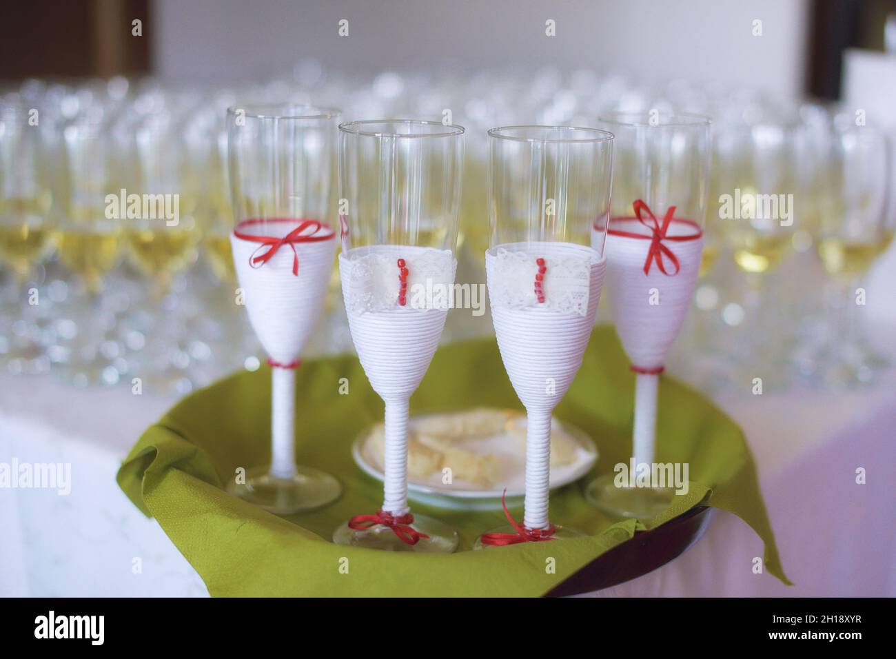 Full glasses of bubbly or champagne with four decorated ones in the foreground set on a green tray selected for bride, groom and witnesses Stock Photo