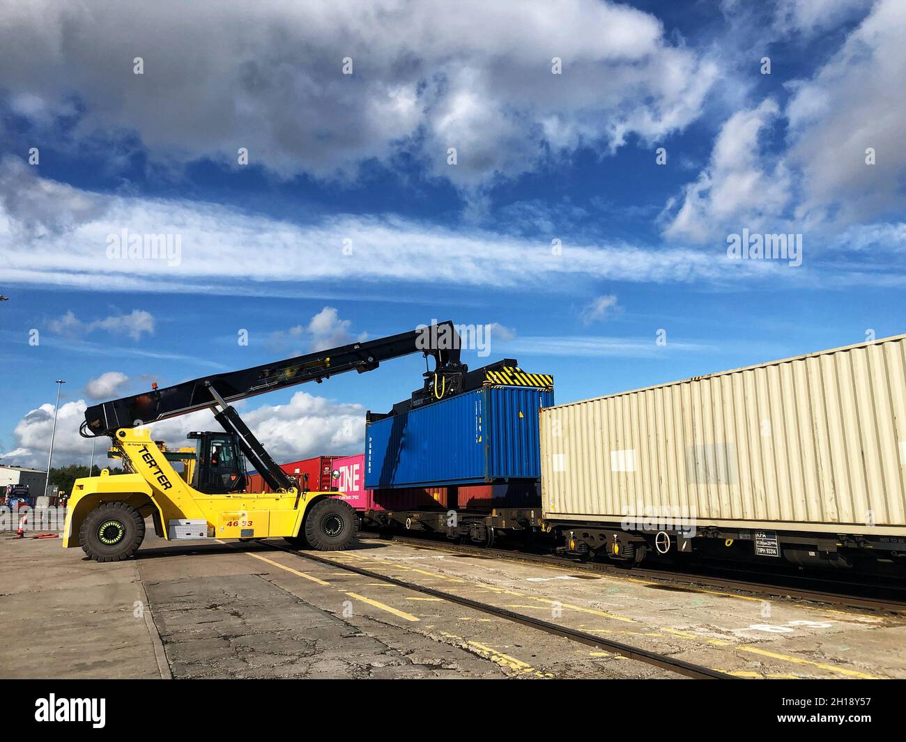 A heavy lifting crane machine loading a shipping container onto a freight train at a commercial terminal port or dock Stock Photo