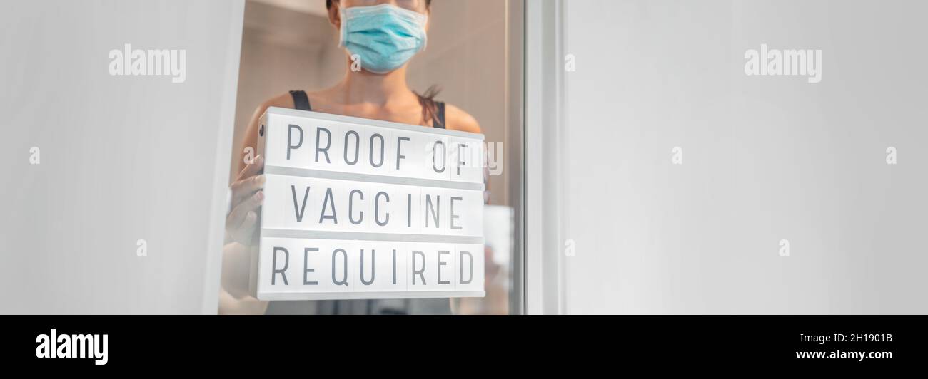 Vaccination proof and mask required to enter stores and non essential businesses as coronavirus restriction. Employe putting requirement sign in Stock Photo