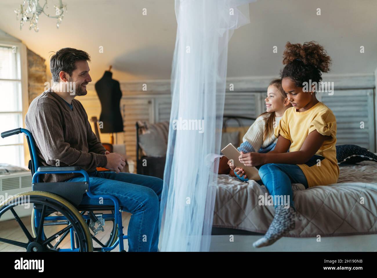 Happy father with disability in wheelchair enjoying time with children at home Stock Photo