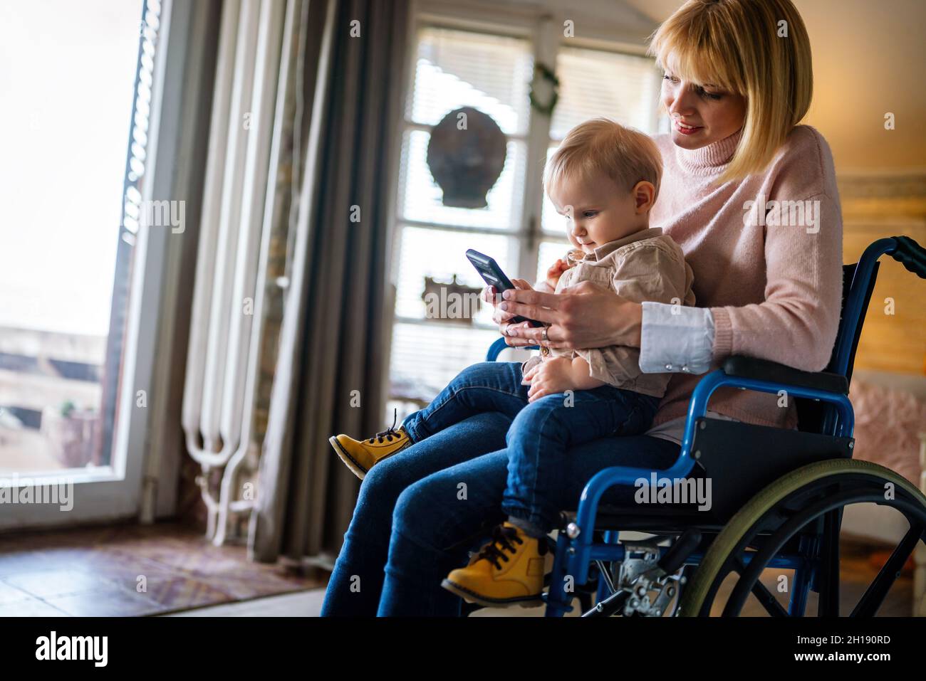 Happy mother in wheelchair with child using digital tablet at home. People family happiness concept. Stock Photo