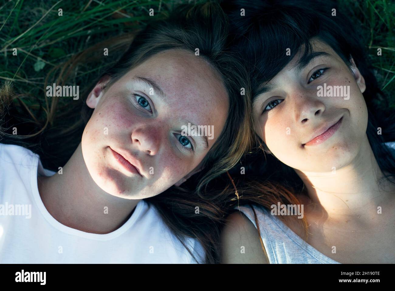 Portrait of two teen girls friends lying on the grass, close-up shot from above. Stock Photo