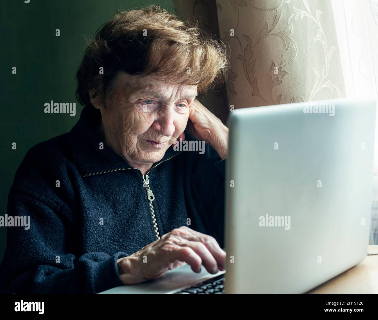 An old woman studying on the computer in her home. Stock Photo